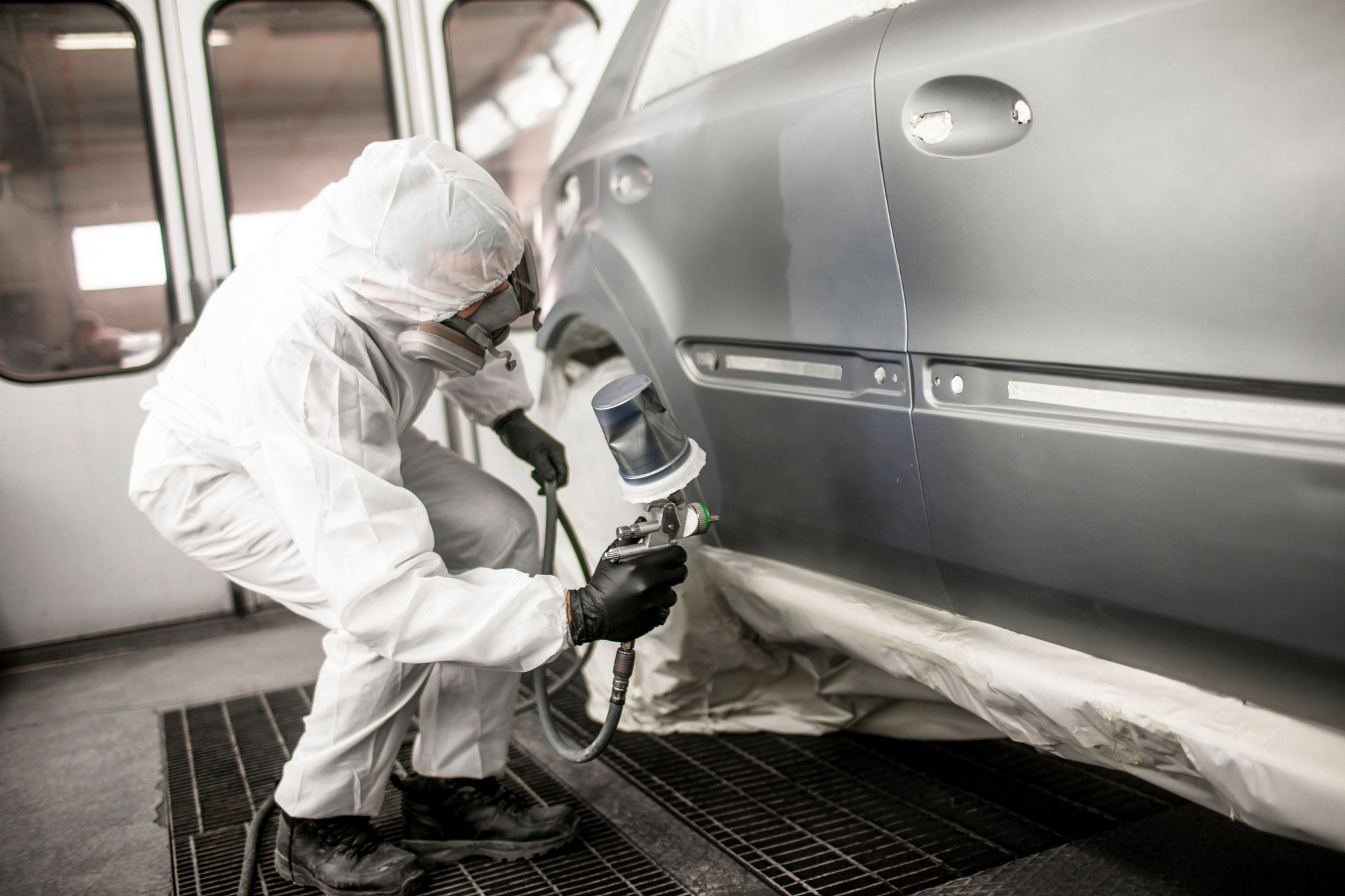 Painting technician applying a coat of paint on a car segment in a body shop painting booth